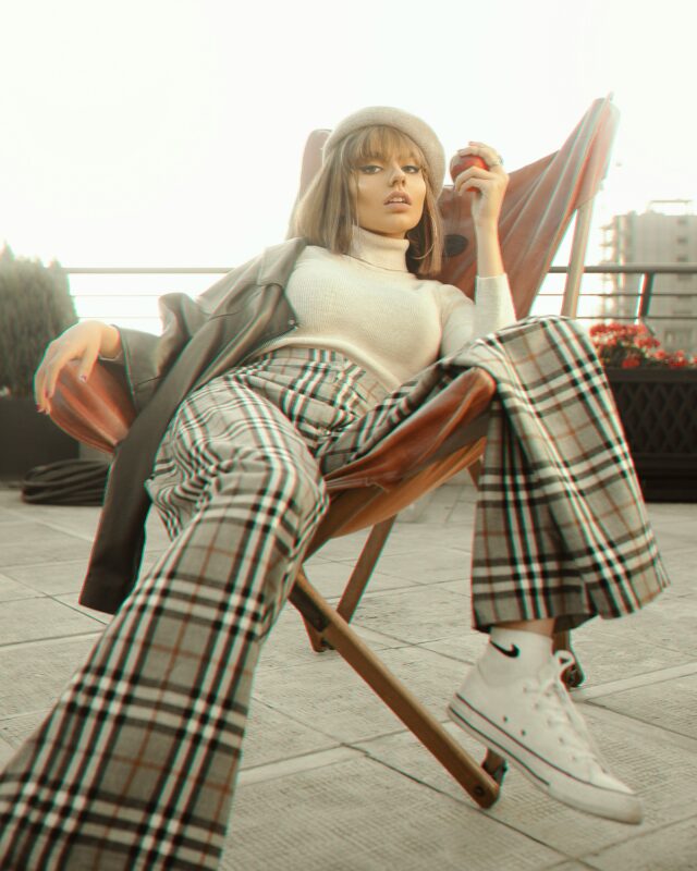 woman wearing a beret, ivory turtleneck, grey coat and plaid trousers with canvas shoes.